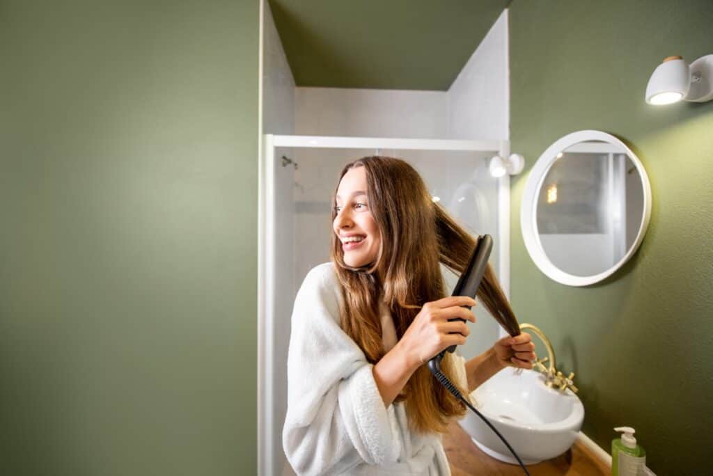 woman straightening hair in the bathroom 2022